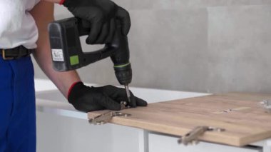 Marangoz mutfak raf kapısının mekanizmalarını (eklemlerini) kurar ve vidalar.