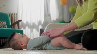 Anne oğlunu kaldırıyor, oturmasına yardım ediyor. Annem bebekle oynuyor. Oturmayı öğreniyor..