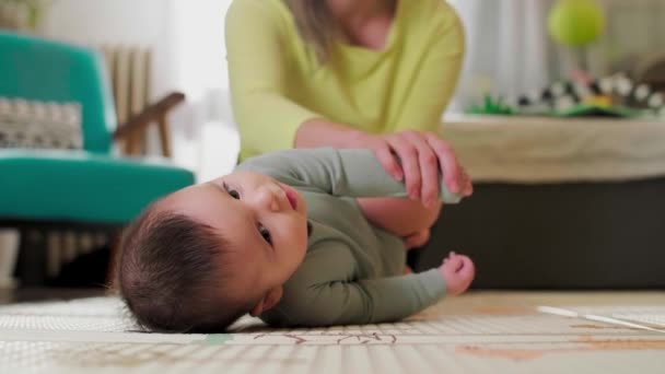 母親は居間で赤ん坊と一緒に運動し 胃の上で転がるのを助けます — ストック動画
