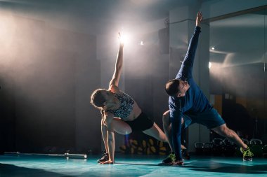 Bir kadın ve bir erkek spor salonunda egzersiz yaparken yana doğru açıyla geriliyorlar..