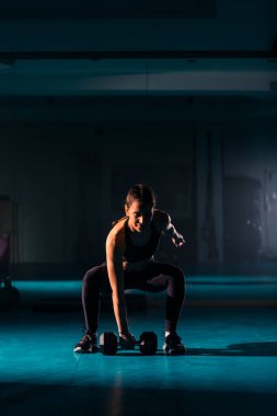 Spor salonunda dambıl kapma egzersizi yapan zinde bir genç kadın..