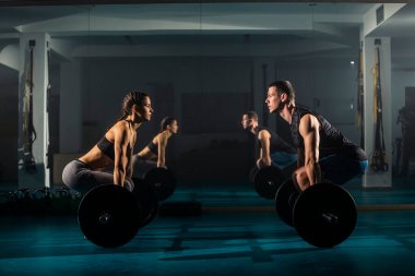 Bir kadın ve bir erkek aynı anda spor salonunda kaldırma egzersizi yapıyor..