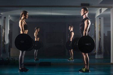 Bir kadın ve bir erkek aynı anda spor salonunda kaldırma egzersizi yapıyor..