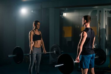 Bir kadın ve bir erkek aynı anda spor salonunda kaldırma egzersizi yapıyor..