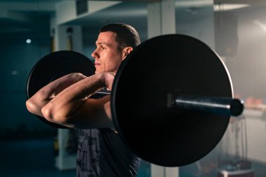 Spor salonunda ağırlıkları üzerinde duran ve halterin ön rafı olarak bilinen egzersiz yapan formda bir adam..