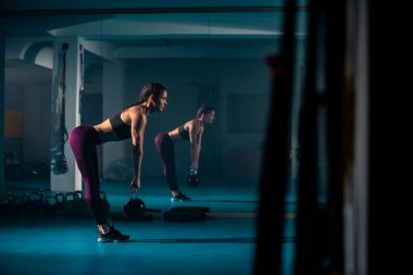 Genç bir kadın spor salonunda ağırlık kaldırma egzersizi yapıyor..