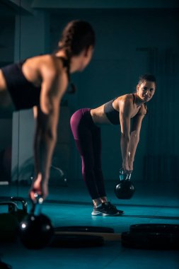 Genç bir kadın spor salonunda ağırlık kaldırma egzersizi yapıyor..