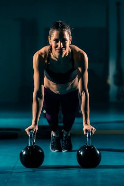Spor salonunda top şeklinde bir ağırlık olan kettlebell 'in yardımıyla şınav çeken genç bir kadın..