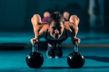 Spor salonunda top şeklinde bir ağırlık olan kettlebell 'in yardımıyla şınav çeken genç bir kadın..