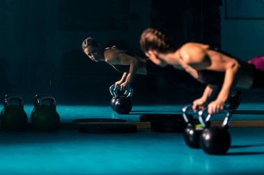 Spor salonunda top şeklinde bir ağırlık olan kettlebell 'in yardımıyla şınav çeken genç bir kadın..