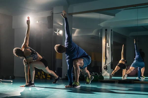 Bir kadın ve bir erkek spor salonunda egzersiz yaparken yana doğru açıyla geriliyorlar..