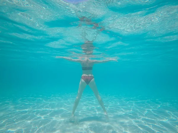 海のターコイズブルーの水の下で泳いでいる女性の体の後部水中ビュー — ストック写真