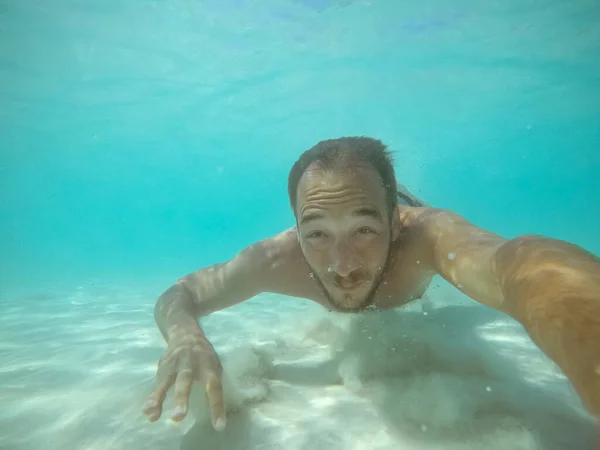 Under water photo of a man diving without equipment in turquoise sea water.