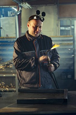 Tamirci, otomatik kaynak aletini işe hazırlarken meslektaşı arkada öğütme işiyle uğraşırken fark edilebilir..