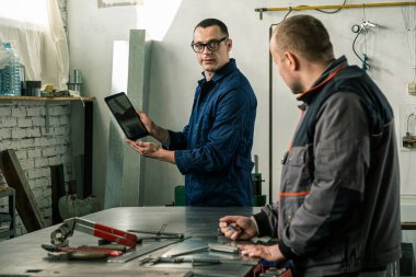 Bir kalaycı ve iş arkadaşı mühendis atölyelerinde birlikte çalışırken, mühendis tablet kullanıyor..