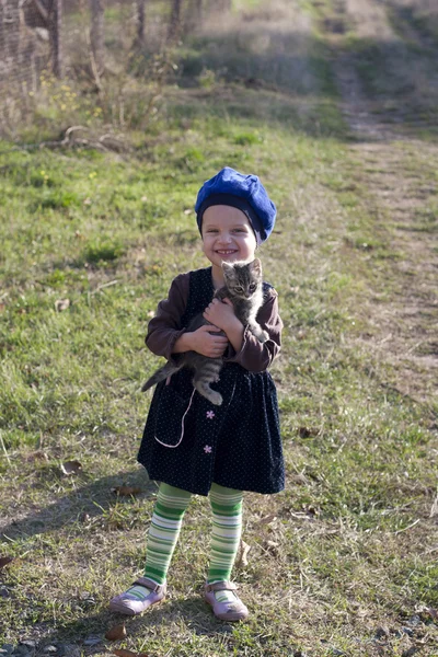 Meisje in een baret glimlacht met een kitten op zijn handen — Stockfoto