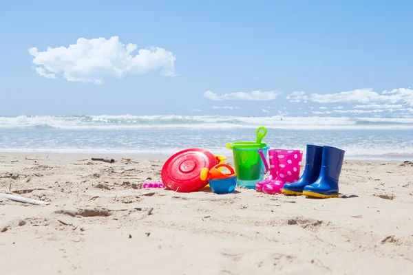 Juguetes de plástico y botas de goma en la arena de la playa — Foto de Stock