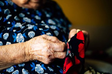 Yaşlı bir kadının elleri kırmızı bir elbise dikiyor. Yakından görülüyor, çok detaylı. Yaşlılık kavramı ve el yapımı bir şey..