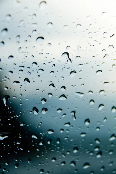 Raindrops on a window seen from close up. Cloudy and bluish day, nice background, could be used as a wallpaper