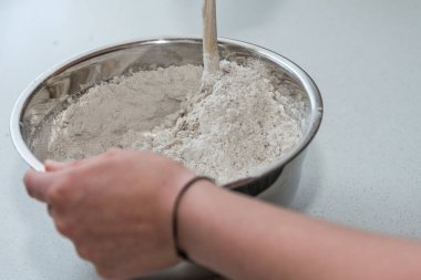 Ekmek pişirmek için unu hamurun içine ahşap bir kaşıkla karıştır. Yakın çekim.