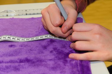 Seamstress with tape measure takes measurements of fabric - close-up