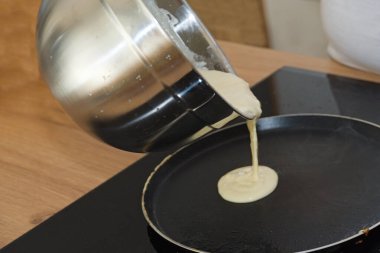 Amatör şef krep hamurunu kızartma tavasına dolduruyor. Yakın plan.