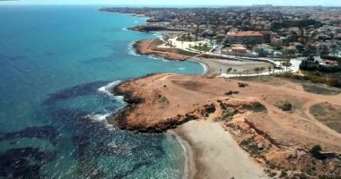 Deniz suyuna, plajlara ve ufukta gezinti güvertesi ve şehir manzarası olan kayalık kıyı şeridine bakan insansız hava aracı görüntüsü..