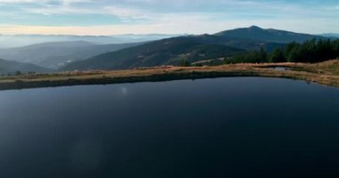 Mavi su gölü üzerinde uçan dron ve dağlarda yer alan çam yeşili orman