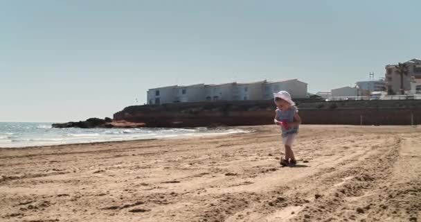 Маленькая девочка бегает по пустому пляжу в один солнечный летний день с видом на море — стоковое видео