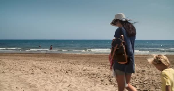Madre e hijos viajan a lo largo de la playa de arena con vistas al mar soleado día de verano — Vídeo de stock