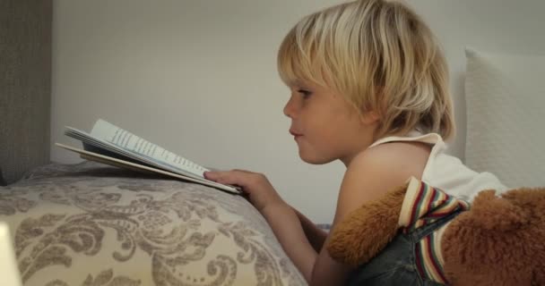 Little boy reading a book before bedtime in his bed on evening — Stock Video