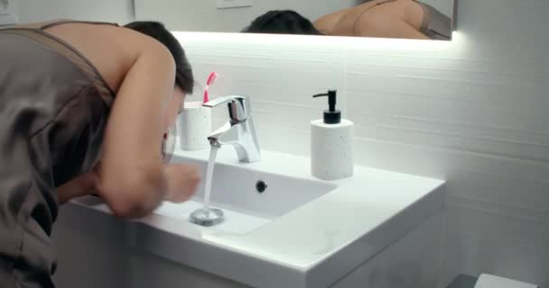 Молодая брюнетка в ночной рубашке умывается перед зеркальной ванной — стоковое видео