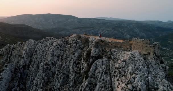 Drone πλησιάζει νεαρό ζευγάρι στην κορυφή του βουνού με ερείπια κάστρο στο ηλιοβασίλεμα — Αρχείο Βίντεο
