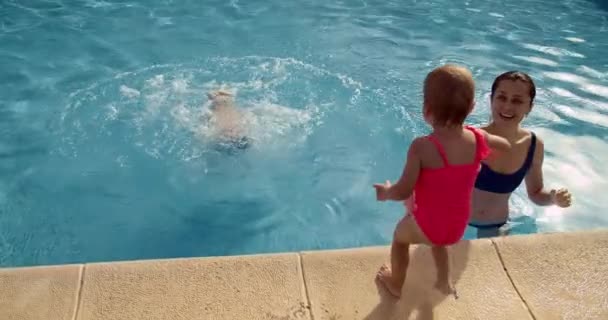 Feliz niño y niña correr y saltar a la piscina de agua azul a su madre — Vídeos de Stock