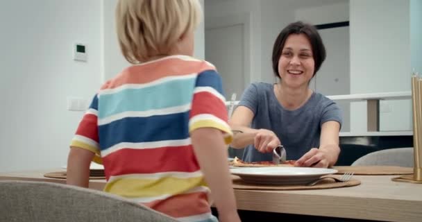 Young beautiful woman cutting pizza and speaking with his son and smiling — Stock Video