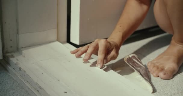 Primer plano de las manos de la mujer joven elimina la pintura seca en la puerta en la mañana soleada — Vídeo de stock