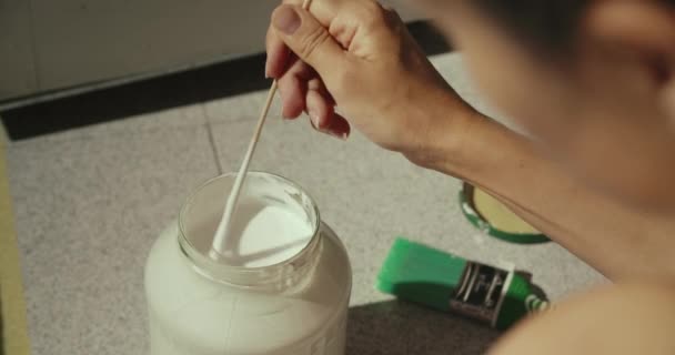 Καυκάσια γυναίκα ανακατεύοντας λευκή μπογιά σε ένα βάζο νωρίς το πρωί — Αρχείο Βίντεο