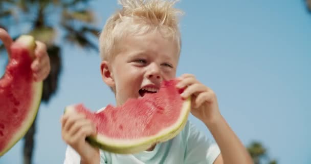 Zbliżenie małego chłopca bawiącego się plasterkiem arbuza i jedzącego go w letni dzień — Wideo stockowe