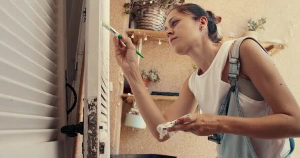 Beautiful young woman painting wooden door with paintbrush in terrace on summer — Stock Video