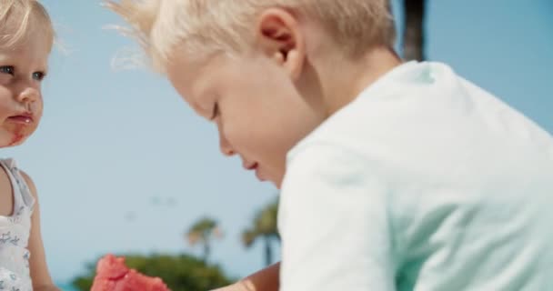 Schöne kleine Junge beißt eine Scheibe Wassermelone an einem klaren, sonnigen Tag — Stockvideo