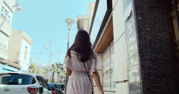 Vista desde la parte trasera de la joven mujer caminando por la calle rápida en la ciudad turística — Vídeos de Stock