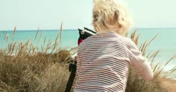 Kleiner Junge spielt mit Vater Stativ im Freien an sonnigem Tag mit Meerblick — Stockvideo
