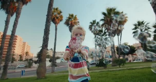 夏の夜に公園で泡のおもちゃの銃で遊んでいる赤ちゃんの男の子と笑顔 — ストック動画