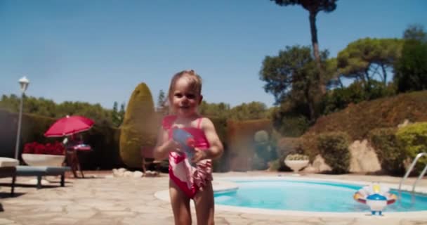 Schattig baby meisje schieten met water pistool direct naar de camera naast het zwembad — Stockvideo