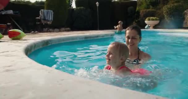 Улыбающаяся мать учит маленькую милую дочь грести и плавать в бассейне. — стоковое видео
