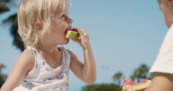Vacker liten flicka biter en bit vattenmelon på en klar solig dag — Stockvideo