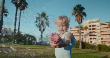 Parkta yeşil çimlerin üzerinde duran baloncuk tabancasıyla oynayan tatlı bir kız.