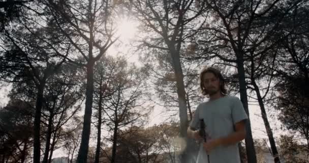 Jonge mannen met brood en lang haar laad geweer en vuur in het bos — Stockvideo