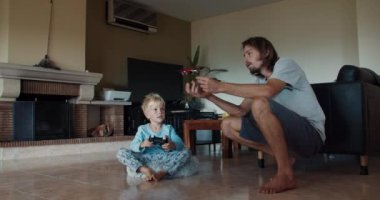 Genç baba ve tatlı erkek çocuk oturma odasında oyuncak kuadkopterle oynuyorlar.