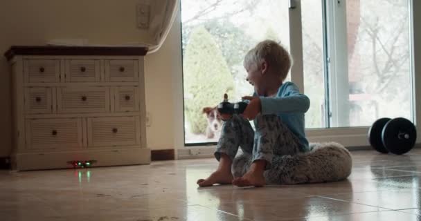 Netter und glücklicher Junge spielt mit Spielzeugdrohne im Wohnzimmer Hund hat Angst — Stockvideo